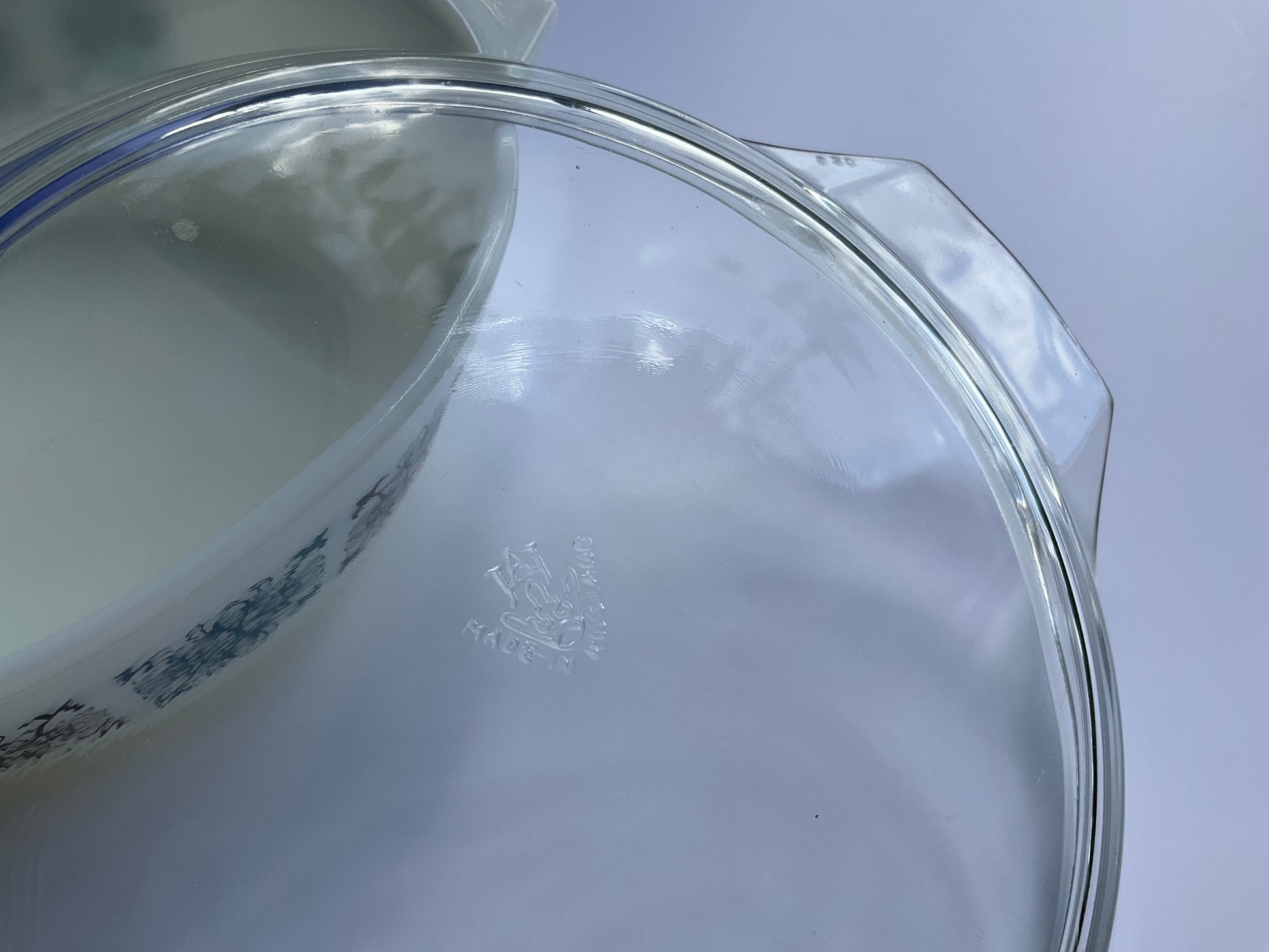 Close up of clear tempered glass Pyrex JAJ oven casserole lid with Chelsea blue and black geometric pattern dish visible through the lid on a white background 