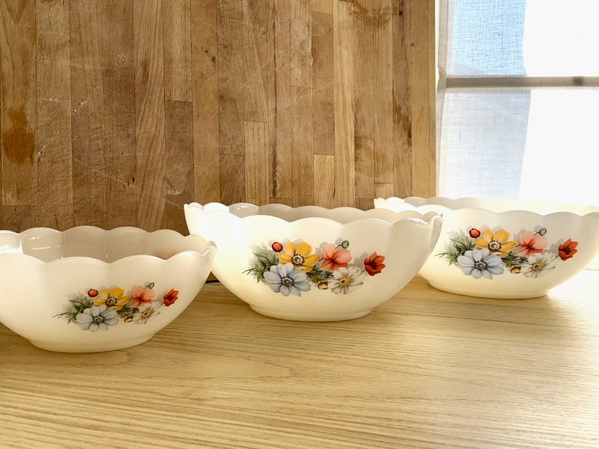 Set of 3 Arcopal scalloped tempered milk glass salad bowls with multicolour anemone flowers pattern. One large, one medium, one small lined up with a wood cutting board background