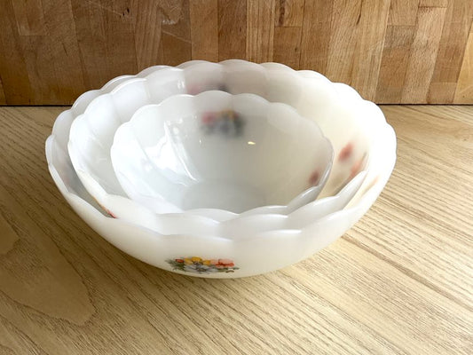 3 Arcopal scalloped tempered milk glass salad bowls with small flowers on the outside. One large, one medium, one small, stacked inside each other on a wood cutting board background