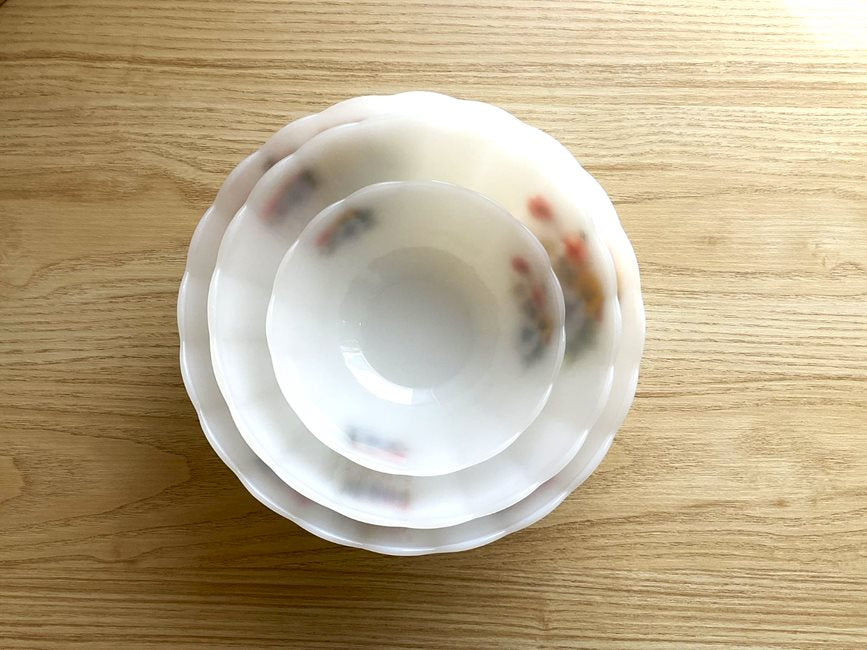 Above view of 3 Arcopal scalloped tempered milk glass salad bowls with small flowers on the outside. One large, one medium, one small, stacked inside each other on a birch  wood background