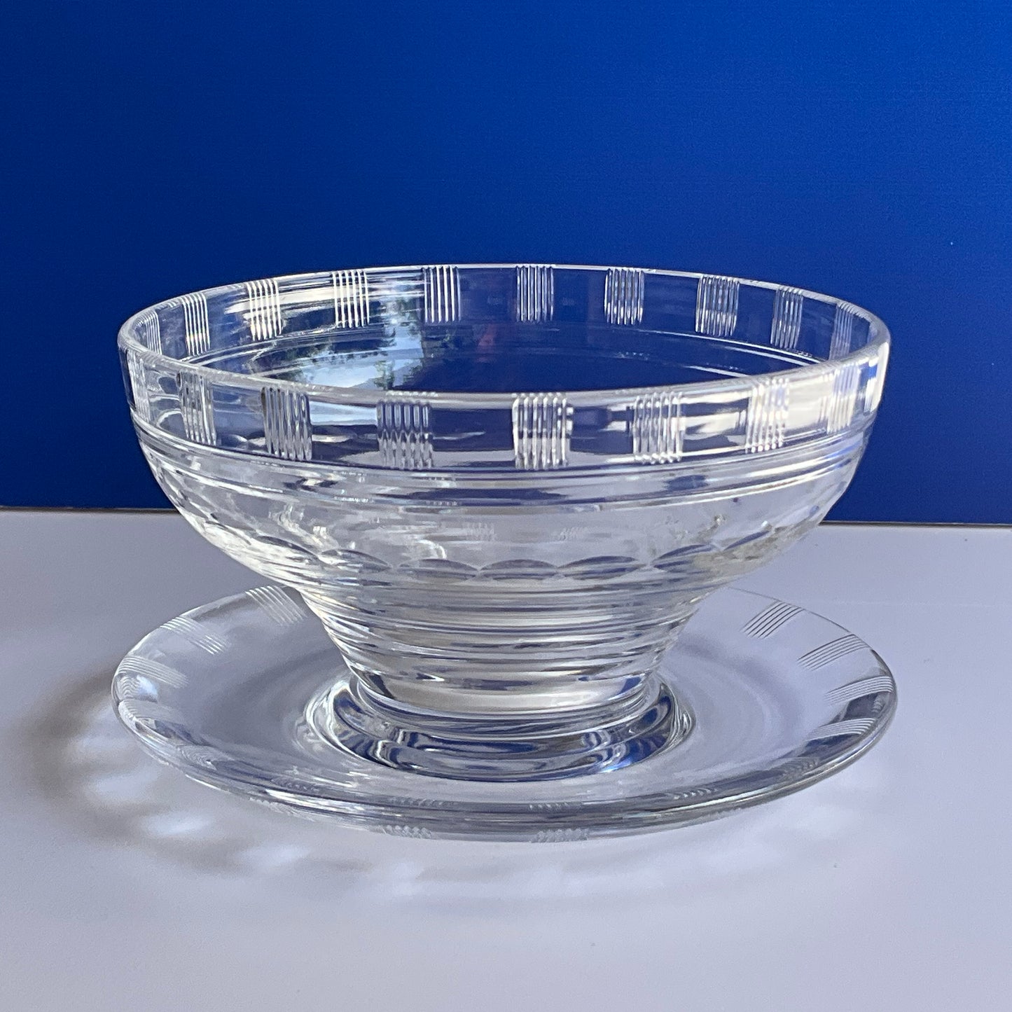 Side view of a clear patterned crystal dessert or appetizer bowl by Stuart England on a blue and white background