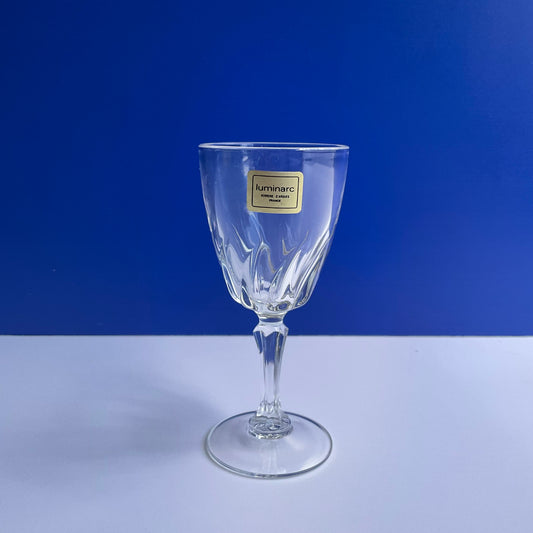 Front view of Luminarc stemmed swirly tempered vine glass with gold label on a blue and white background