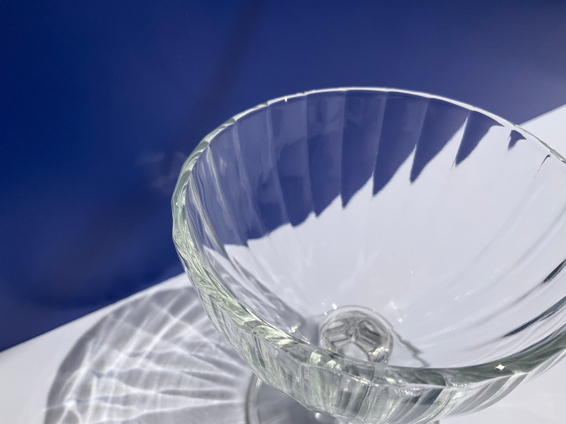 Close up of the rim of a clear tempered glass Arcoroc France stemmed clear dessert cup on blue and white background