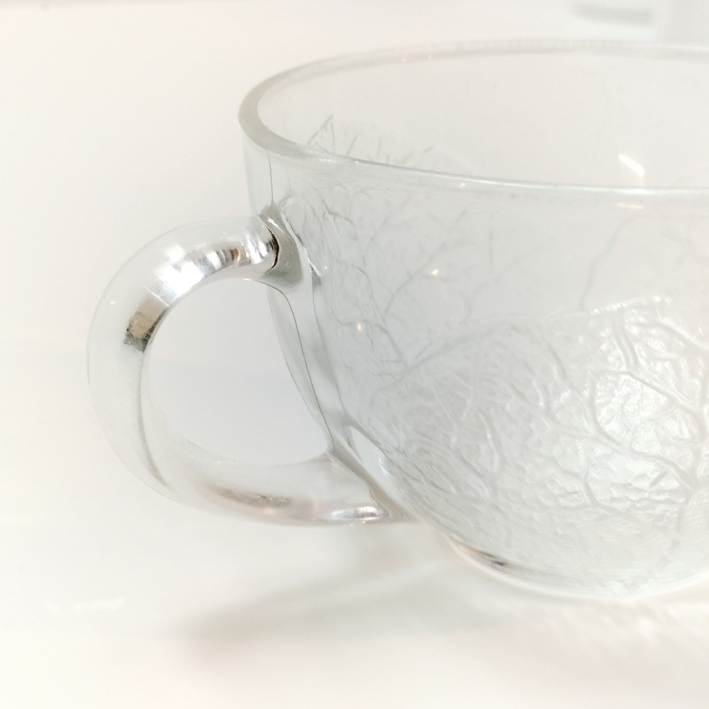 Close up of Arcoroc Aspen clear tempered glass coffee cup with leaf pattern on white background