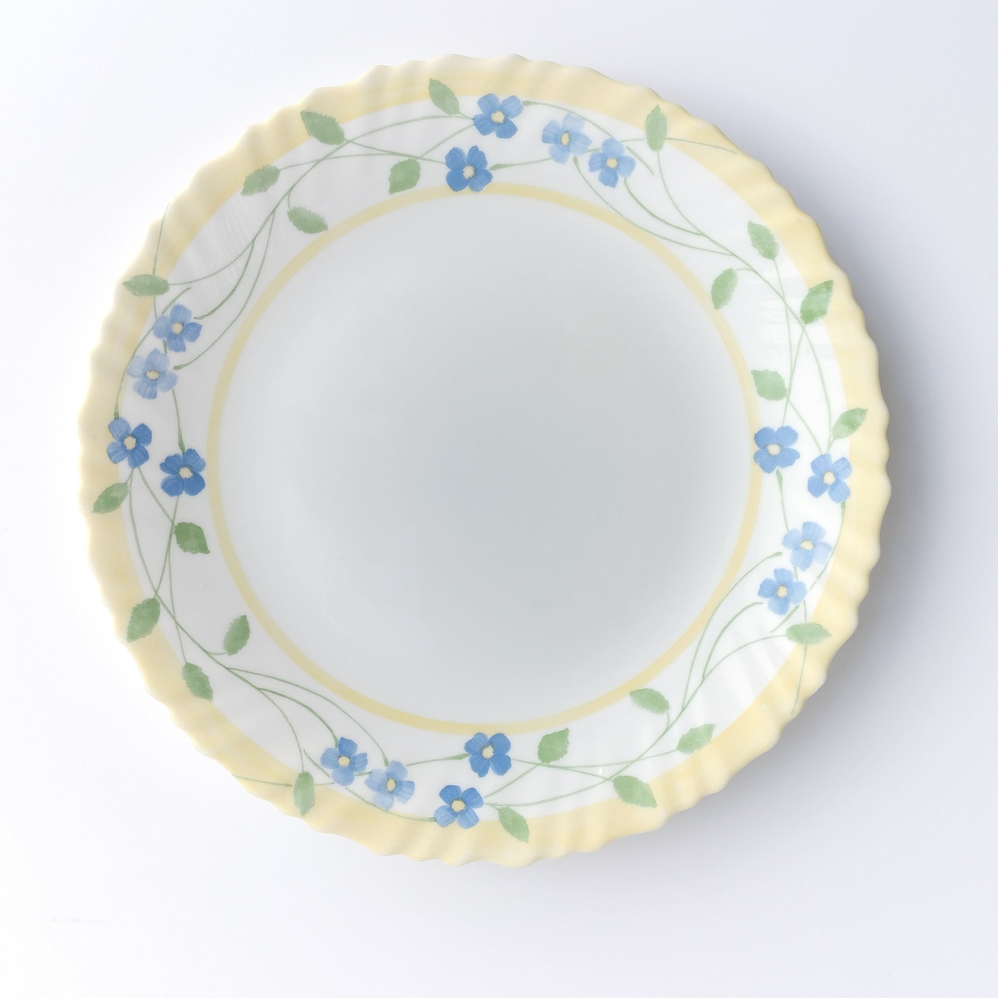 White tempered milk glass dinner plate with blue flower on yellow fluted rim by Arcopal France on a white background