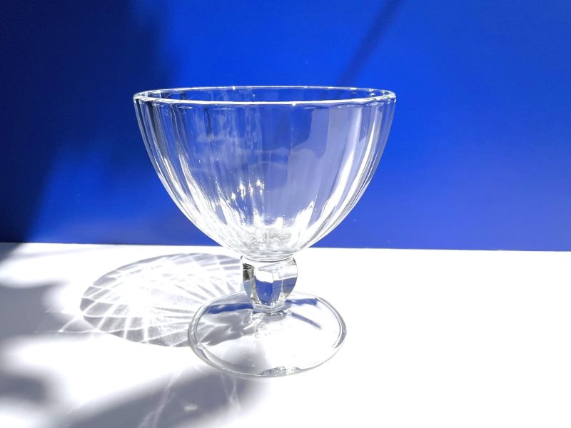 Centered front view of a clear tempered glass stemmed dessert cup by Arc France on a blue and white background